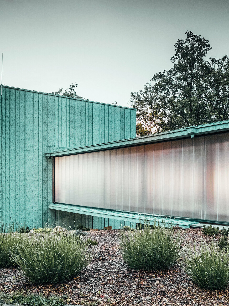 Das Zero Magnetic Field Laboratory in Fertőboz (HU) ist umhüllt von PREEFALZ in der Farbe P.10 Patinagrün. Das würfelförmige Laborgebäude durch einen Tunnel mit dem Nebengebäude verbunden. Die Seitenwände des Durchgangs verleihen dem Bauwerk eine Transparenz durch ihre Milchglasfolierung. Im Hintergrund ist die natürliche Landschaft im Licht des Sonnenuntergangs zu sehen. 