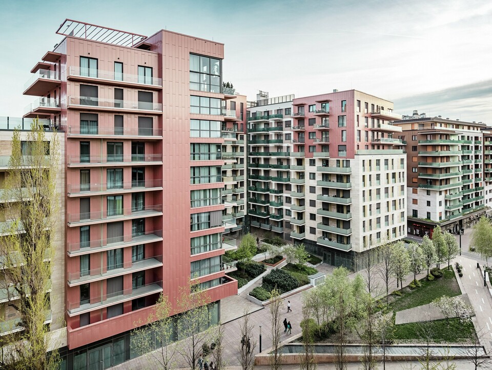 Panoramaaufnahme des Grand Corvin Wohnkomplexes im neugestalteten Corvin-Viertels in Budapest. Die markanten Gebäudeteile sind mit über 800 m² PREFA Siding Fassadenpaneelen in vertikaler Verlegung und Sonderfarbe Lachsmetallic versehen. Die langlebige Aluminiumverkleidung setzt architektonische Highlights, fügt sich harmonisch in die urbane Struktur ein und unterstreicht den hochwertigen, zeitgemäßen Charakter der neuen Wohnanlage entlang der Corvin-Promenade.