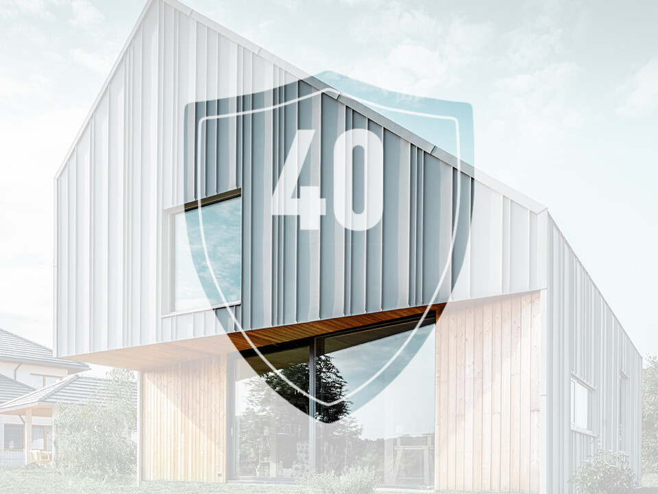 A képen a PREFA alumínium termékekre vonatkozó garanciát jelképező „40” számmal ellátott tábla látható egy modern családi ház előtt.