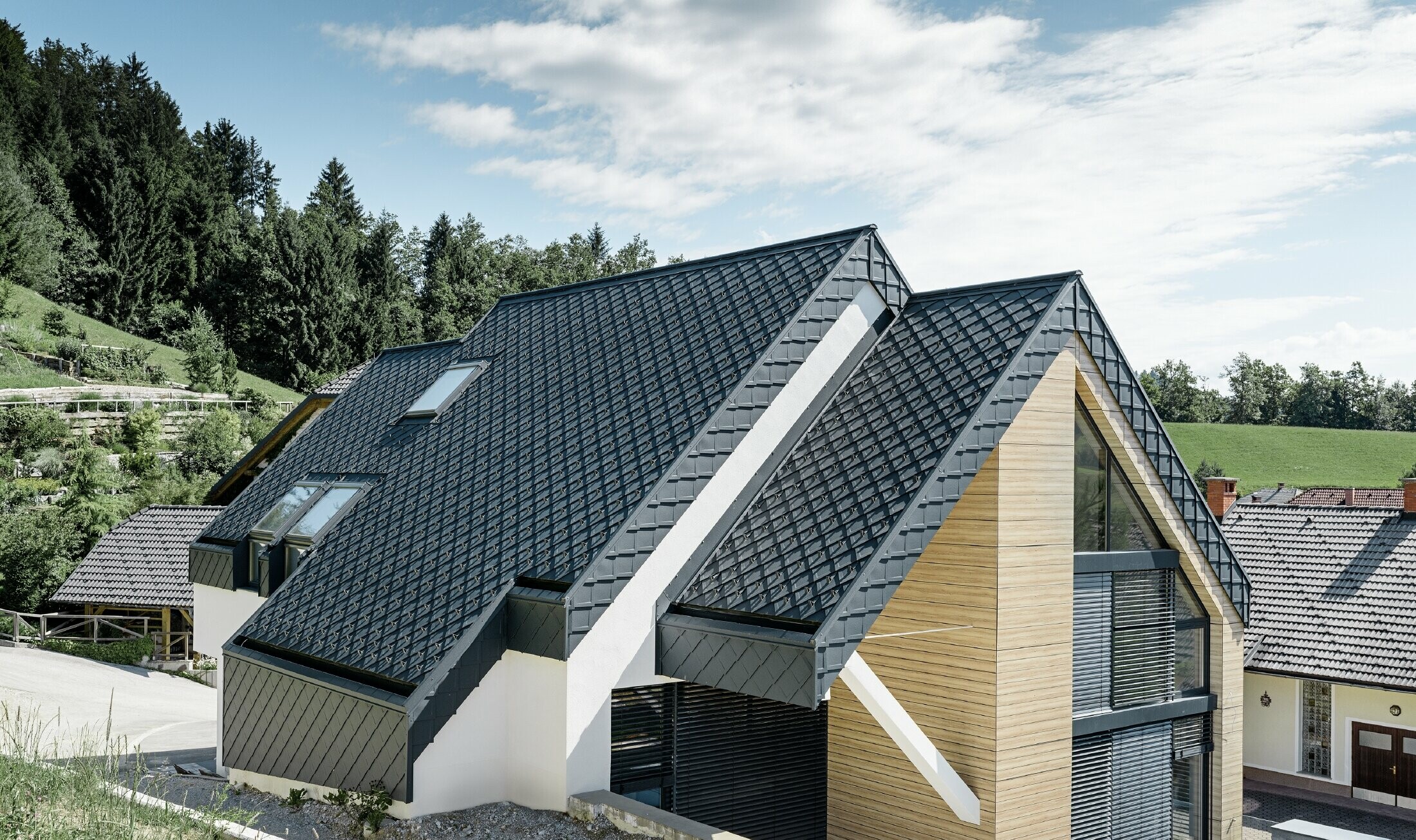 Nyeregtetős családi ház tetőtúlnyúlás nélkül, fahatású homlokzattal, antracitszínű alumínium tetővel