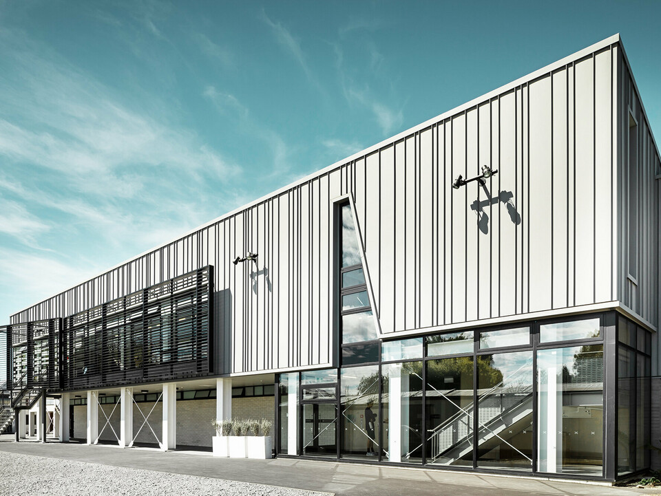 Die Vorderseite des neuen, von Wilkie + Bruce entworfenen St Andrew's College Fitnesscenters aus der seitlichen Perspektive: Seine Verglasung und die linierte, patinagraue Aluminiumfassade mit Einschnitt sind im Fokus, darüber erstreckt sich der Himmel.