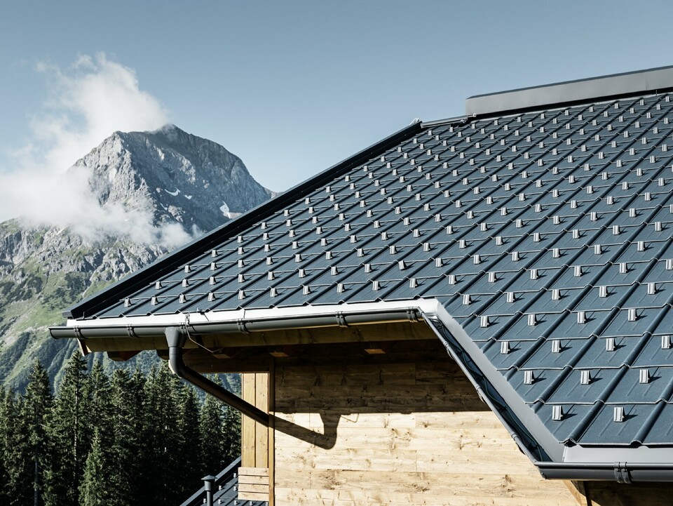 Faház a hegyekben, a tetőt PREFA Classic elem borítja antracit színben PREFA ereszcsatornával és fa homlokzattal