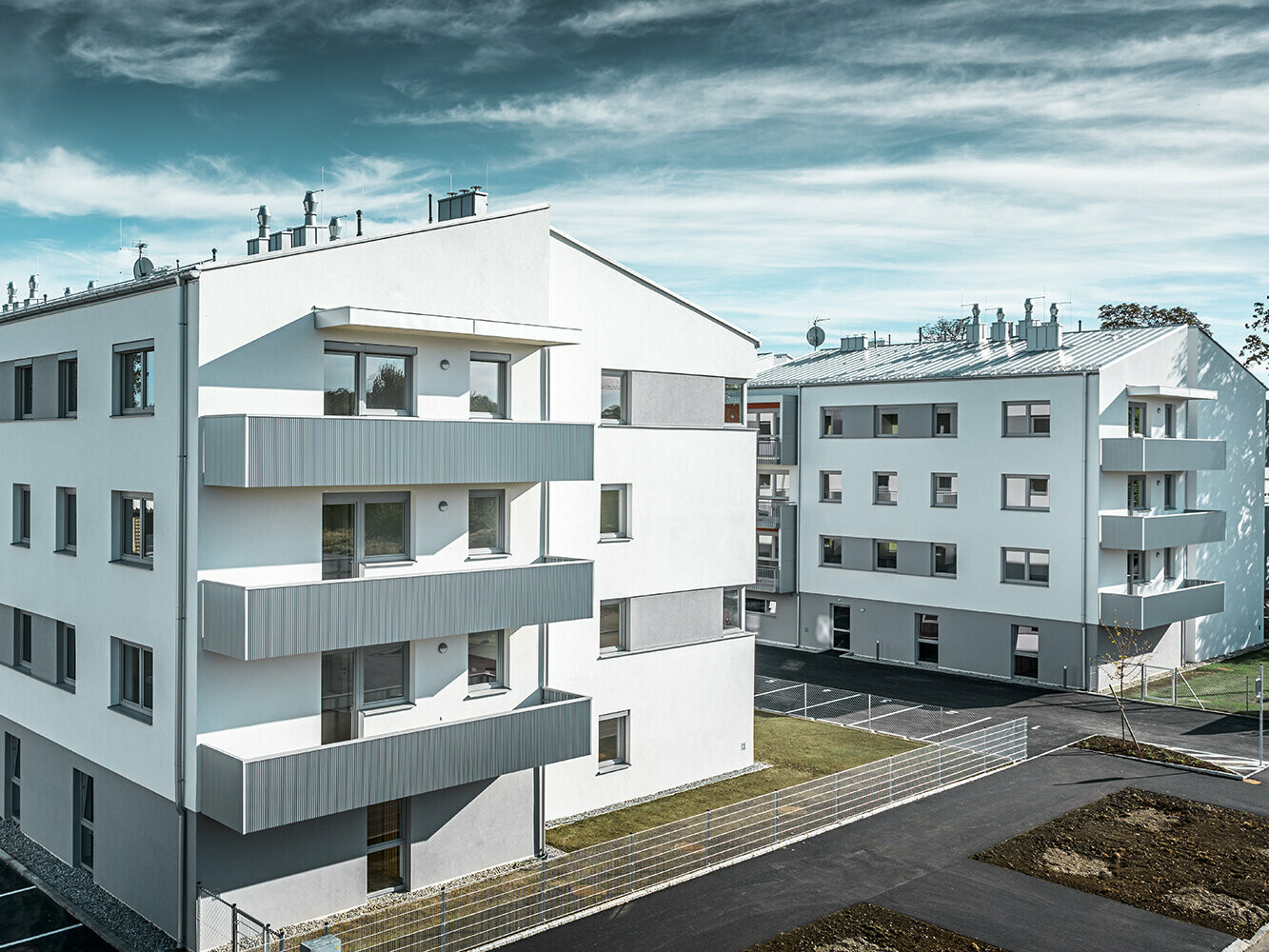 Modern lakókomplexum fehér homlokzattal és PREFA fogazott profilú erkéllyel, ezüstmetál színben