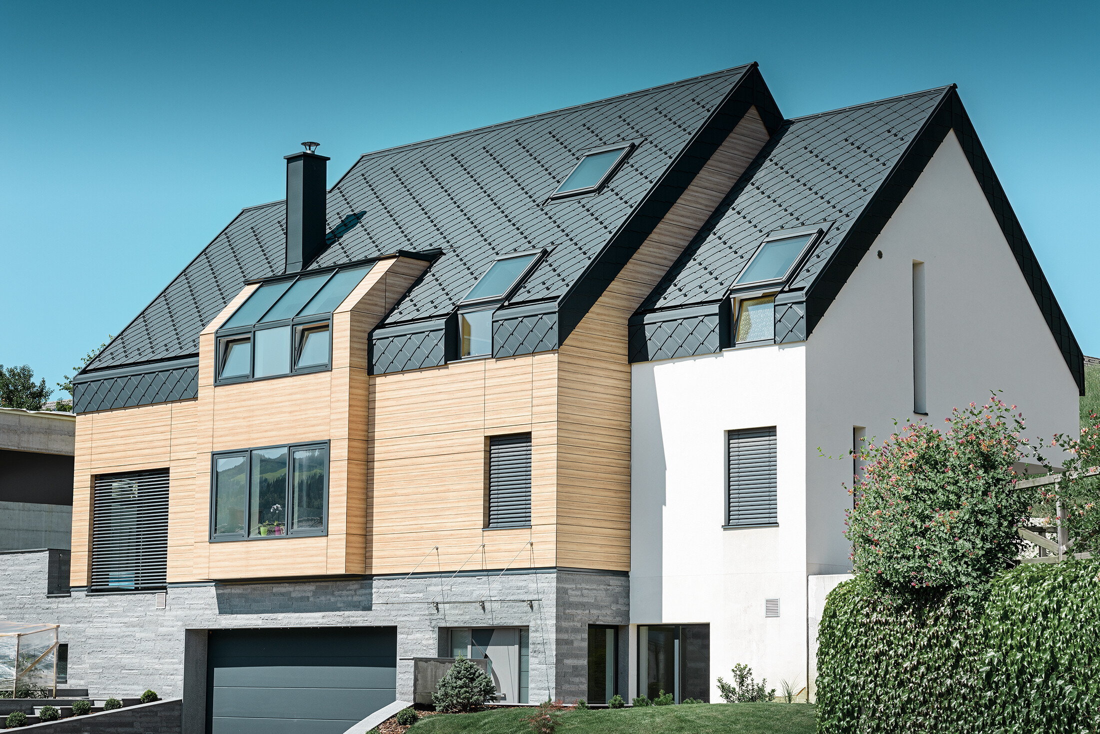 Korszerű új épület, ahol a tetőhéjazat a homlokzat felső része fölé is kinyúlik, tetőhéjazatként az antracitszínű alumínium tetőfedő rombuszt használták