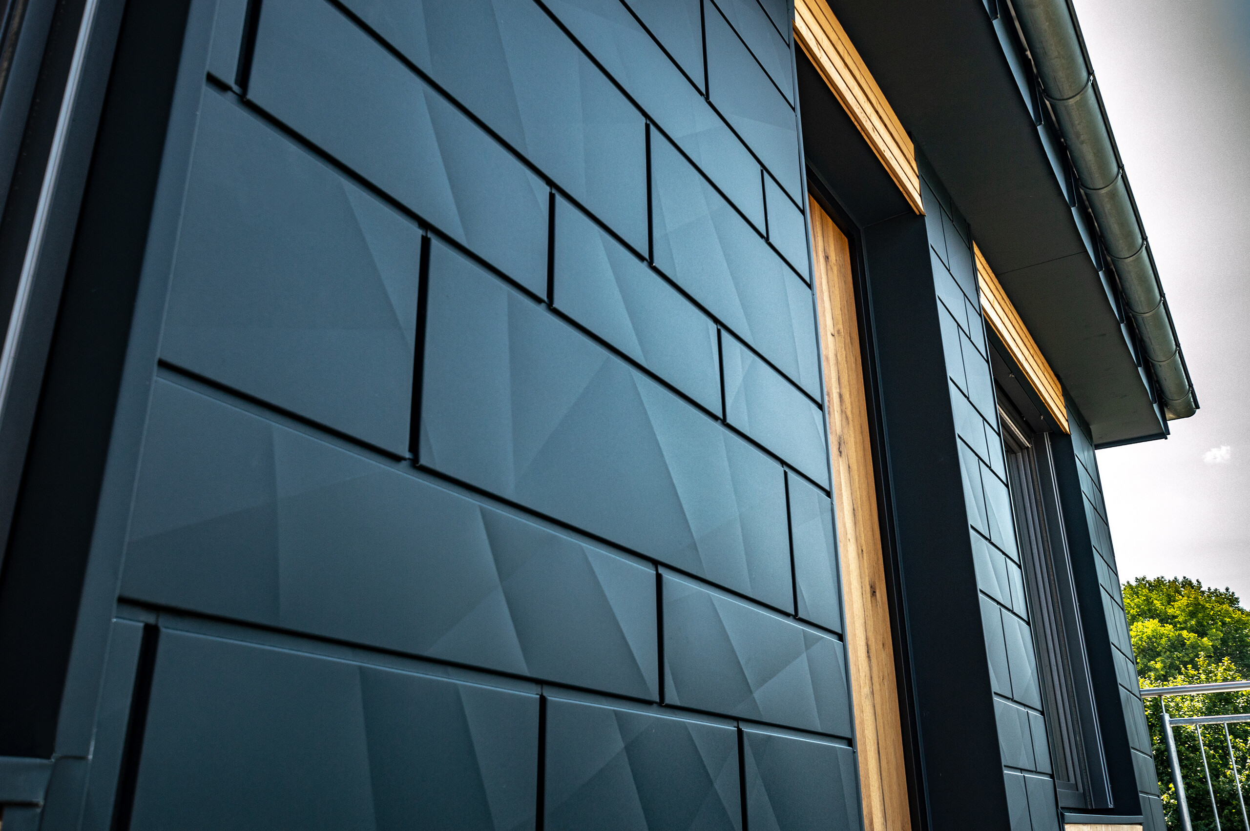 Homlokzat PREFA Siding.X antracit színben, erkélyajtókkal és nagy üvegfelületekkel, fahomlokzattal keverve.