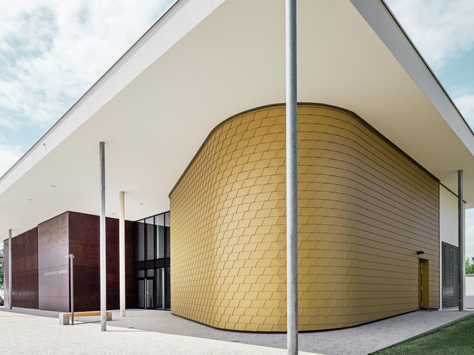 Seitliche Aufnahme der Landesmusikschule in Buchkirchen. Die Fassade wurde mit PREFA Wandschindeln in der Sonderfarbe Mayagold verkleidet.