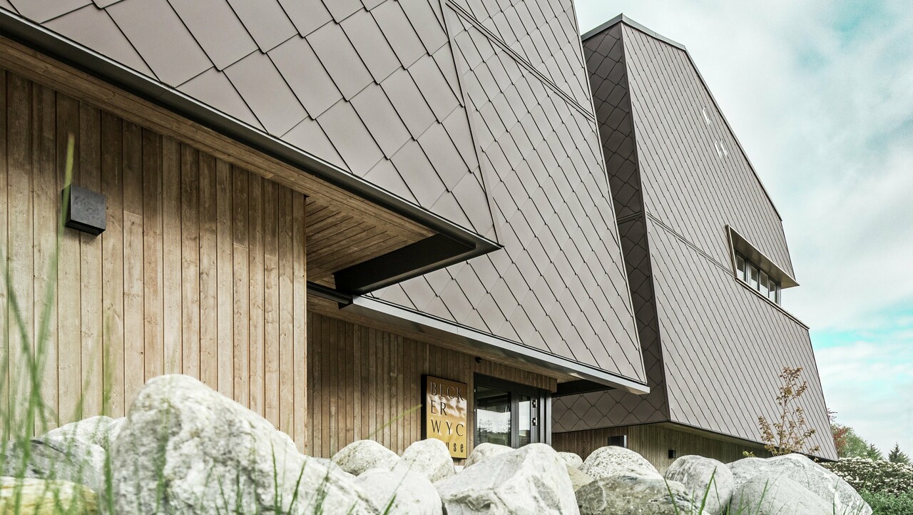 Oldalnézet a szállodából, a földszint homlokzatát függőlegesen sötét színű fával burkolták. E fölött egy homlokzati kiugrás található, innen a homlokzatot dióbarna színű alumíniumpanelekkel burkolják.