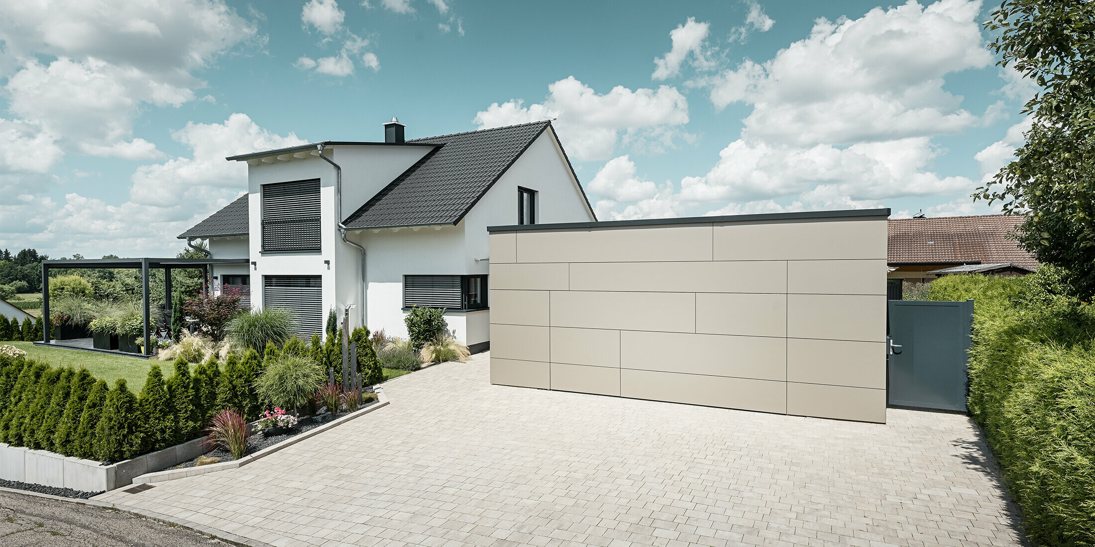 Die Garage des Einfamilienhauses ist an der Fassade komplett mit der Aluminium Verbundplatte in Bronze verkleidet. Auch das Garagentor ist mit den Fugen nicht erkennbar. Davor ist eine großzügige Einfahrt. 