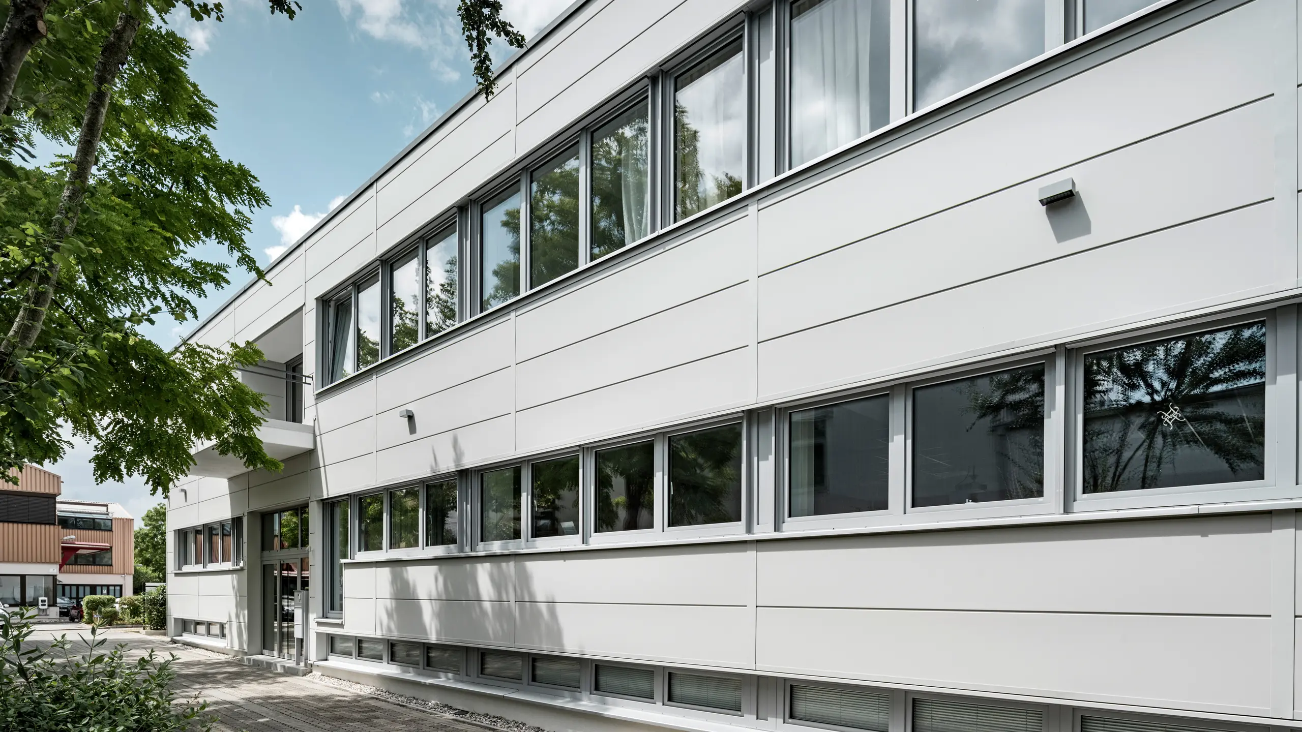 Großformatige PREFA Sidings umhüllen ein Firmengebäude in Oberschleißheim (Deutschland). Die extrabreiten Fassadenelemente aus Aluminium sind in der Farbe Prefaweiß gehalten.