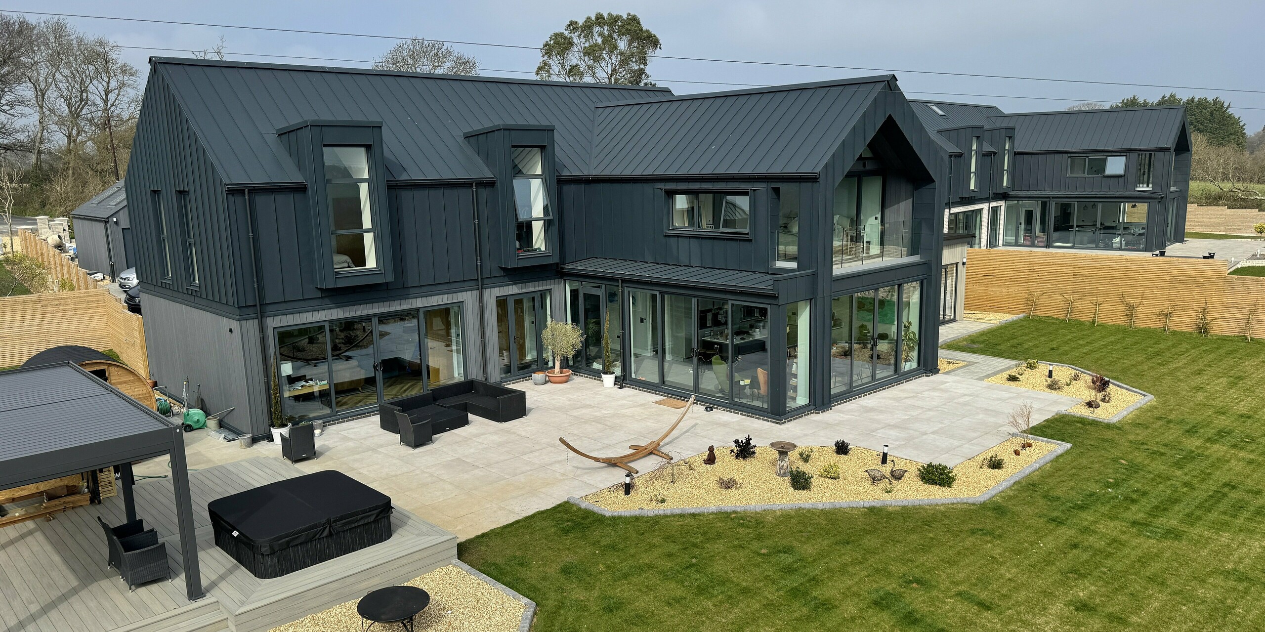 Zwei moderne Einfamilienhäuser auf der Isle of Wight mit markanter PREFALZ Dach- und Fassadenverkleidung in P.10 Dunkelgrau. Die klare Linienführung und die großzügigen Glasfronten schaffen ein lichtdurchflutetes Ambiente. Die Aluminiumoberflächen sind korrosionsbeständig, langlebig und wartungsarm – ideal für die Küstenlage. Unterschiedliche Materialien im Erdgeschoss setzen subtile Akzente und verleihen dem Ensemble Individualität. Die Kombination aus zeitgemäßer Architektur und hochwertigen PREFA Produkten macht dieses Projekt zu einem echten Eyecatcher.