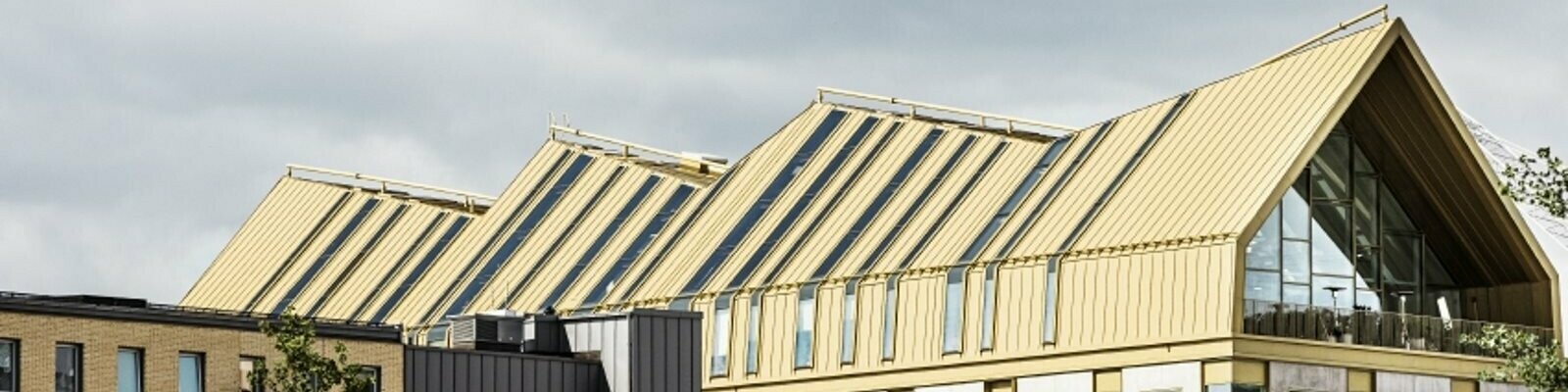 seitliche Frontansicht des Gebäudes in Malmö eingedeckt mit dem Dachsystem PREFALZ in der Sonderfarbe Jaisalmer Gold