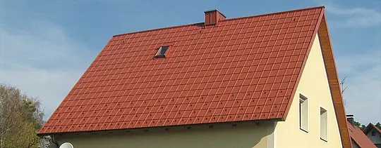 Klasszikus nyeregtető kis tetőablakkal és kéménnyel, PREFA téglavörös tetőlemezzel fedve, hófogókkal és tetőbiztonsági horoggal.