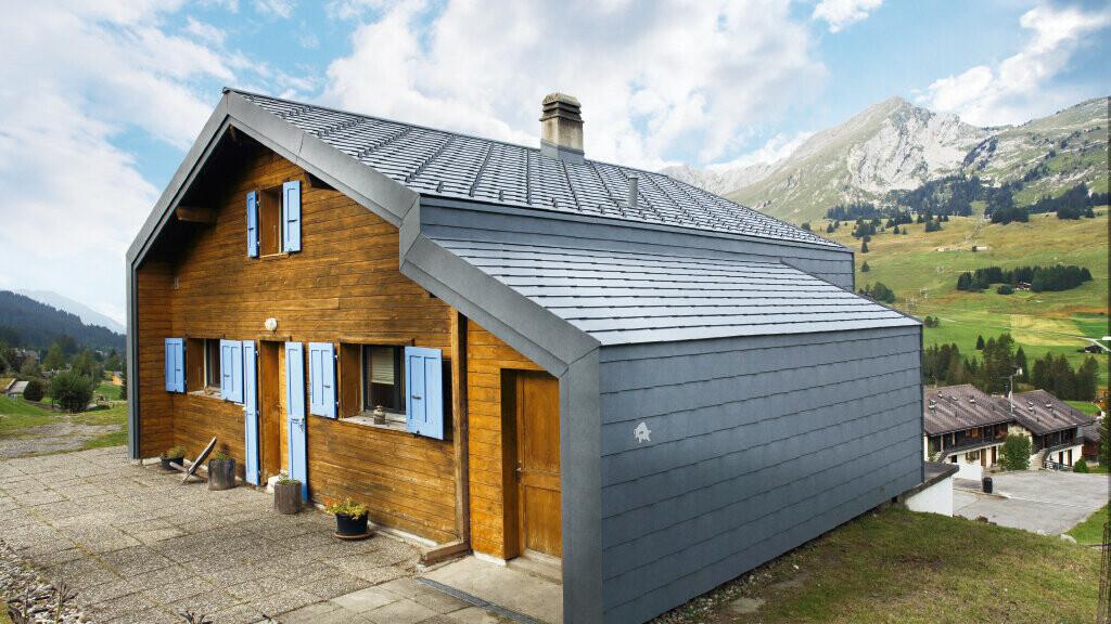 Ház a svájci hegyekben fa homlokzattal, kombinálva a PREFA tetőfedő- és homlokzatburkoló rombusszal márványszürke színben
