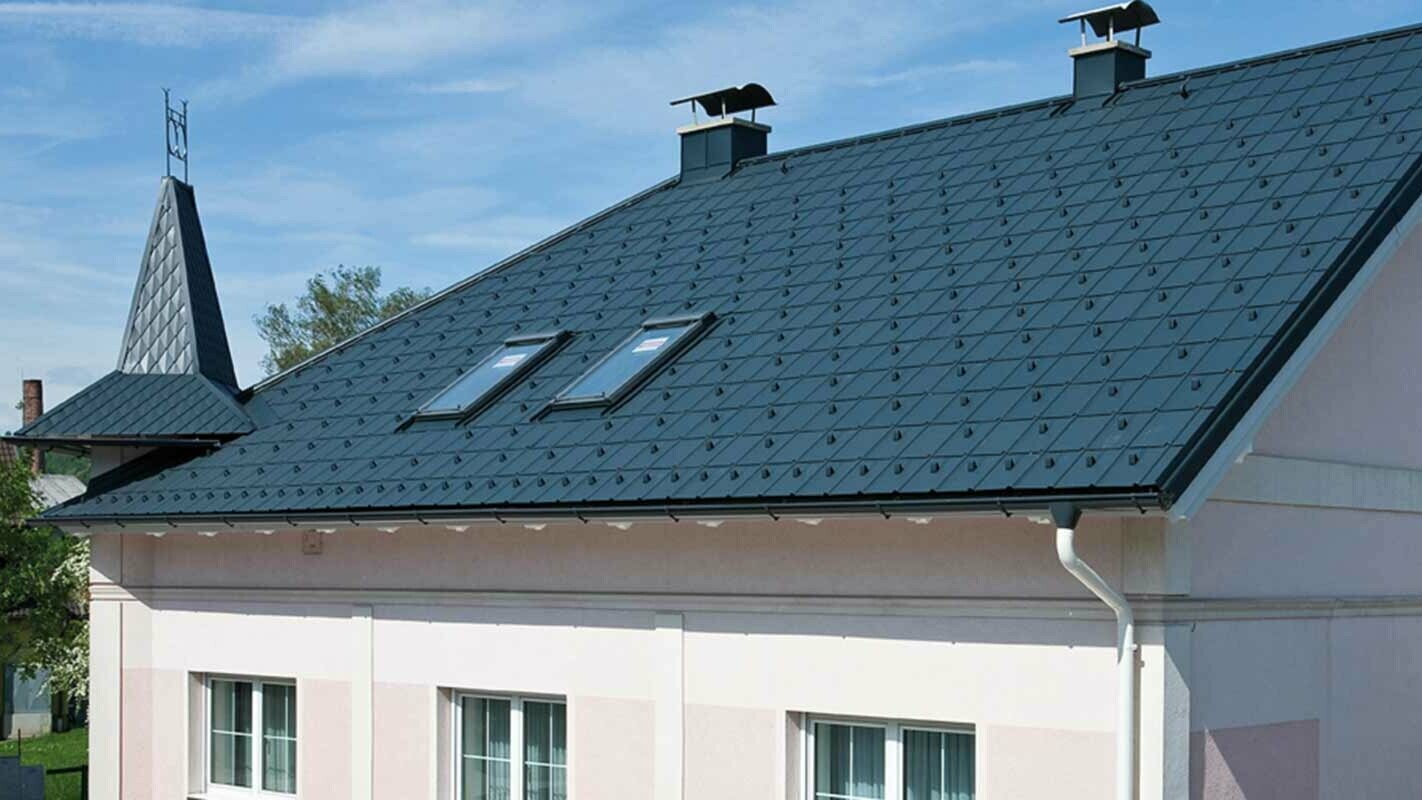 Társasház tetőfelújítás után, PREFA Classic elem, Ausztria – előtte eternit szálcement, kisebb tornyok és rózsaszín homlokzat