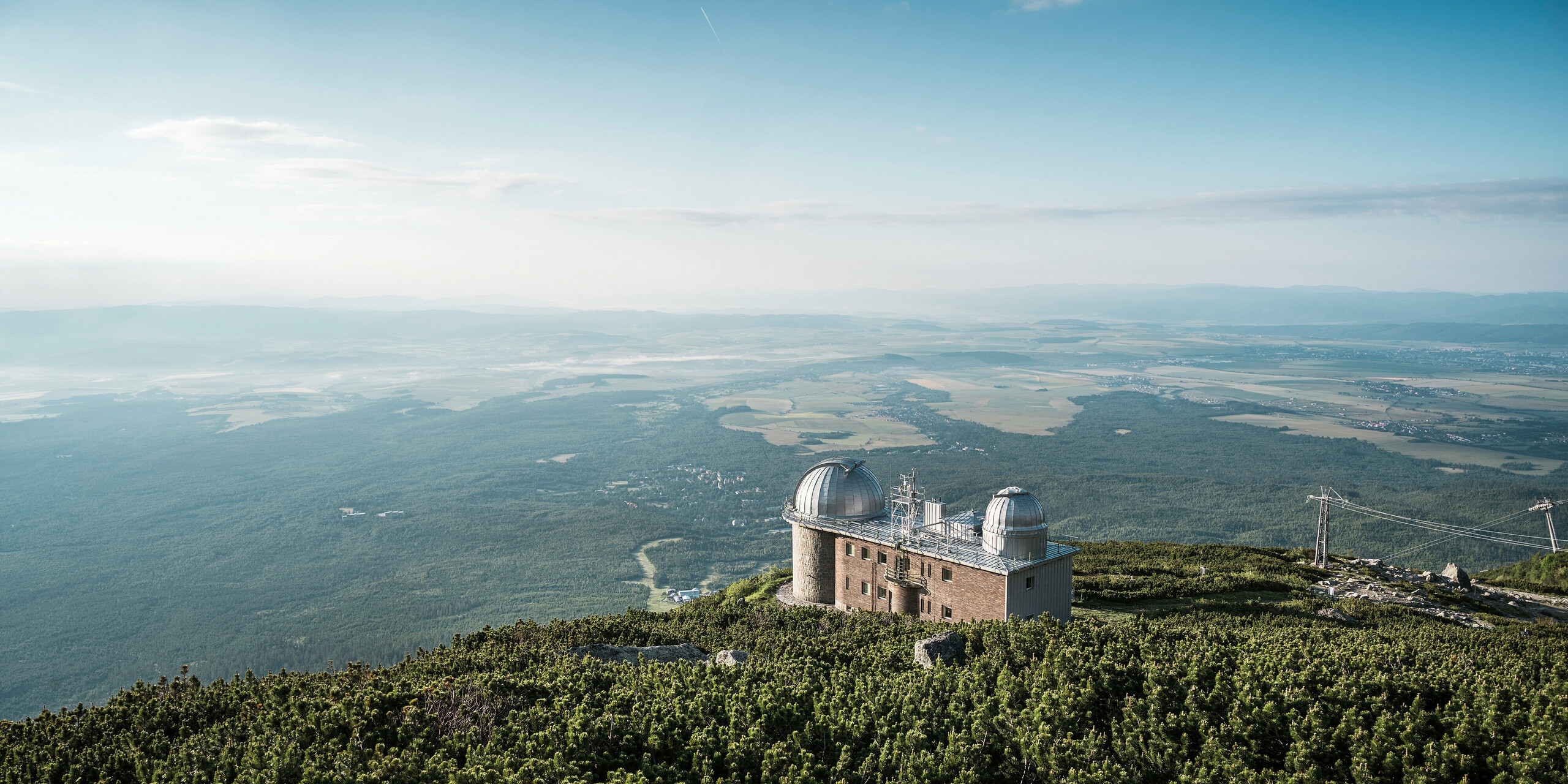 Atemberaubende Fernsicht von der Sternwarte Skalnate Pleso, die auf einer Höhe von 1 783 m liegt, umgeben von der friedlichen Pracht der Hohen Tatra in der Slowakei. Die beiden charakteristischen Kuppeln, die mit silbermetallisch glänzendem PREFALZ verkleidet sind, spiegeln die Weite des Himmels wider und harmonieren mit der Natur. Das Observatorium steht nicht nur für astronomische Spitzenleistungen, sondern auch für die Langlebigkeit und ökologische Stärke von PREFA, dessen Aluminiumprodukte selbst in dieser abgelegenen Höhe Schutz und Haltbarkeit bieten und für die eine umfassende Garantie von 40 Jahren gilt.