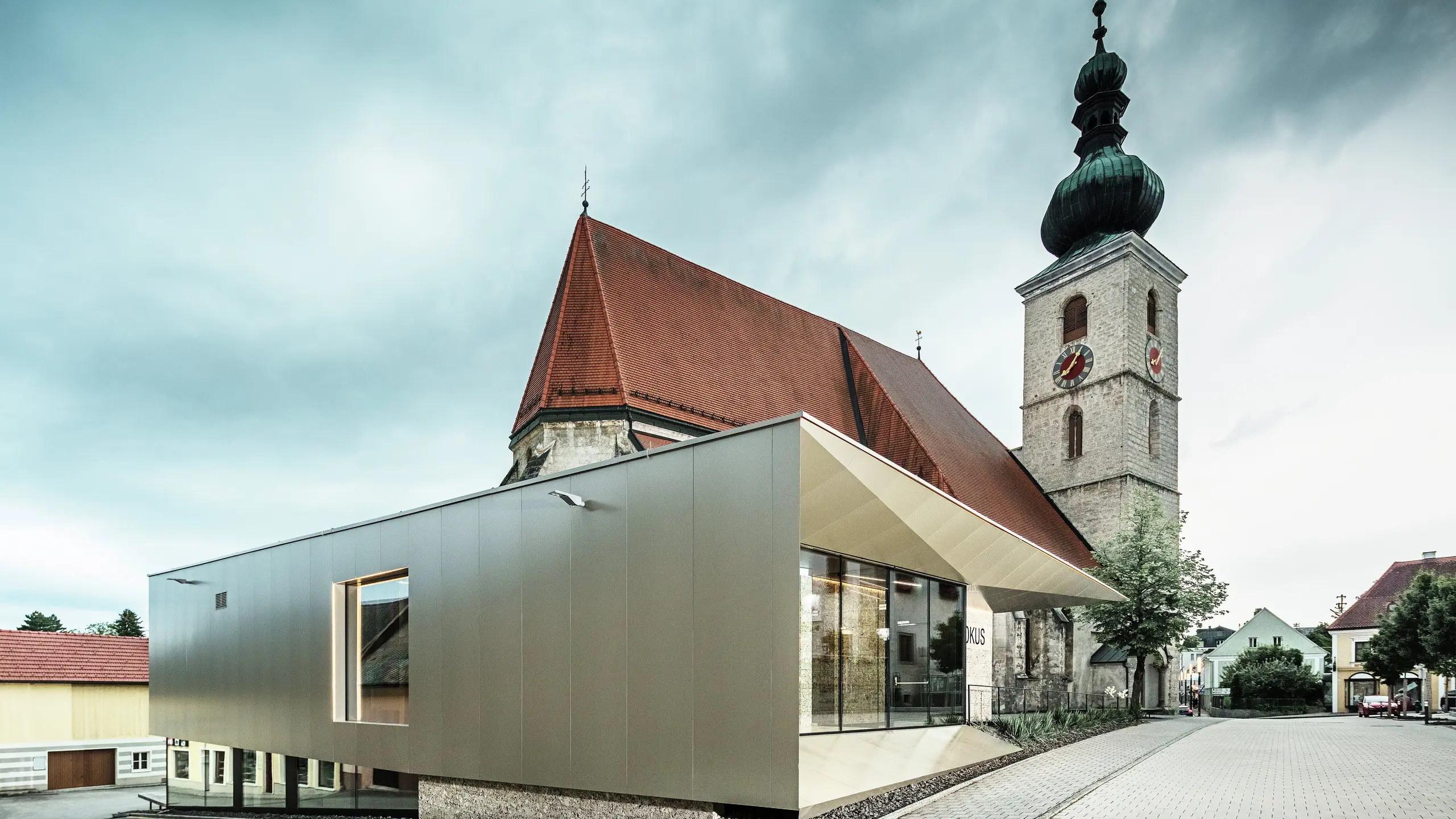Az oldalnézet a filigrán tetőkiugrást mutatja, amely kiváló minőségű PREFA alumínium kompozit lemezzel készült. A precíz kivitelezés modern megjelenést kölcsönöz a tiszta vonalaknak, és hangsúlyozza az építészeti kapcsolatot a régi és az új között.