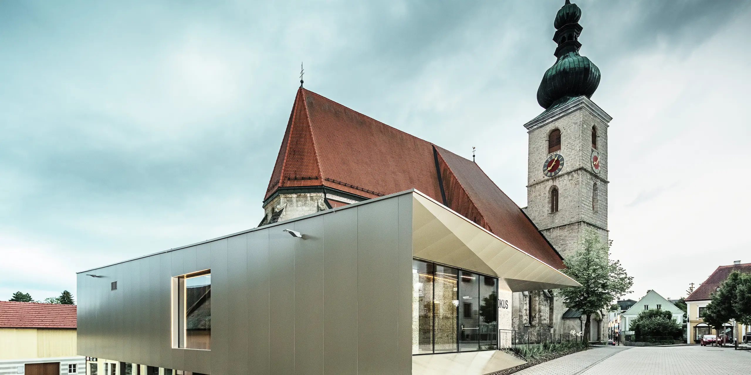 Az oldalnézet a filigrán tetőkiugrást mutatja, amely kiváló minőségű PREFA alumínium kompozit lemezzel készült. A precíz kivitelezés modern megjelenést kölcsönöz a tiszta vonalaknak, és hangsúlyozza az építészeti kapcsolatot a régi és az új között.