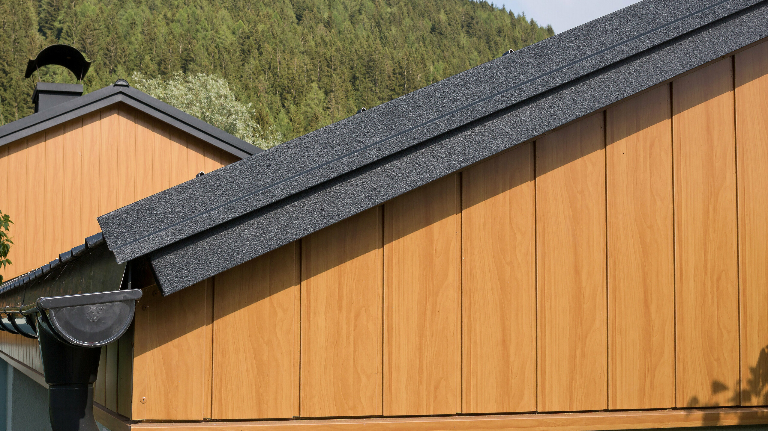 Oromfalburkolat függőlegesen felszerelt natúr tölgy PREFA alumínium Siding elemekkel és antracit ereszcsatornával.