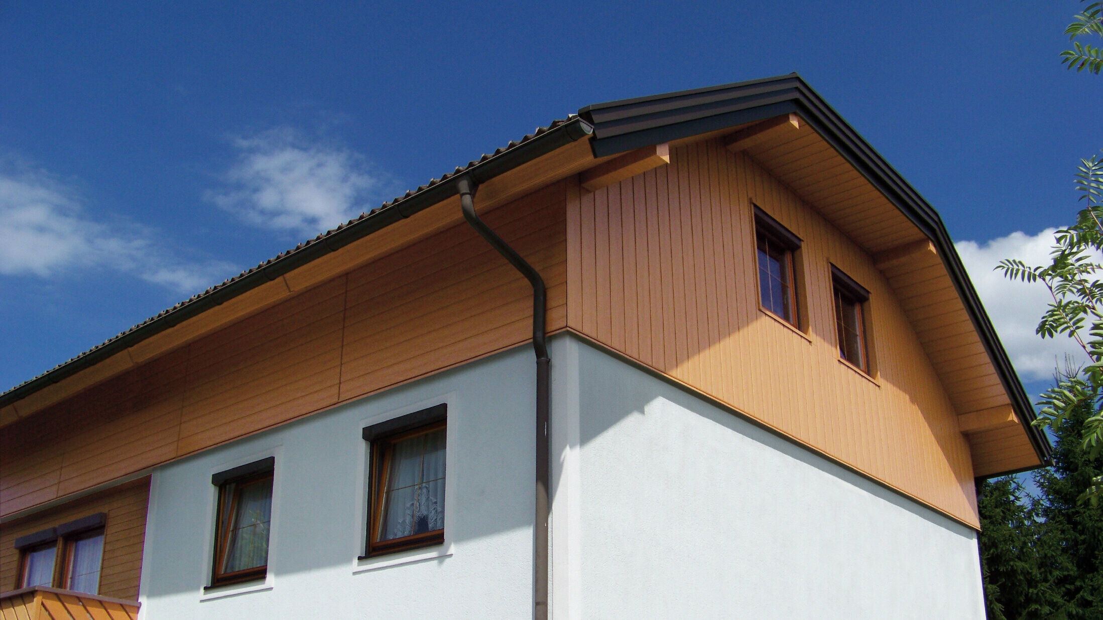 Nagy családi ház téglánytetővel és ormótlan kereszttetővel, PREFA Sidings fagerincelés a homlokzaton fa hatású kivitelben (tölgy természetes színben)