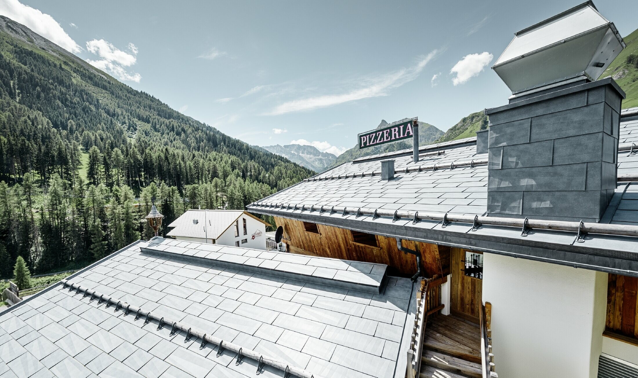 Almrausch étterem Bergennel a háttérben és márványszürke színű PREFA FX.12 tetőfedő panel fedéssel, hófogórönk tartókkal