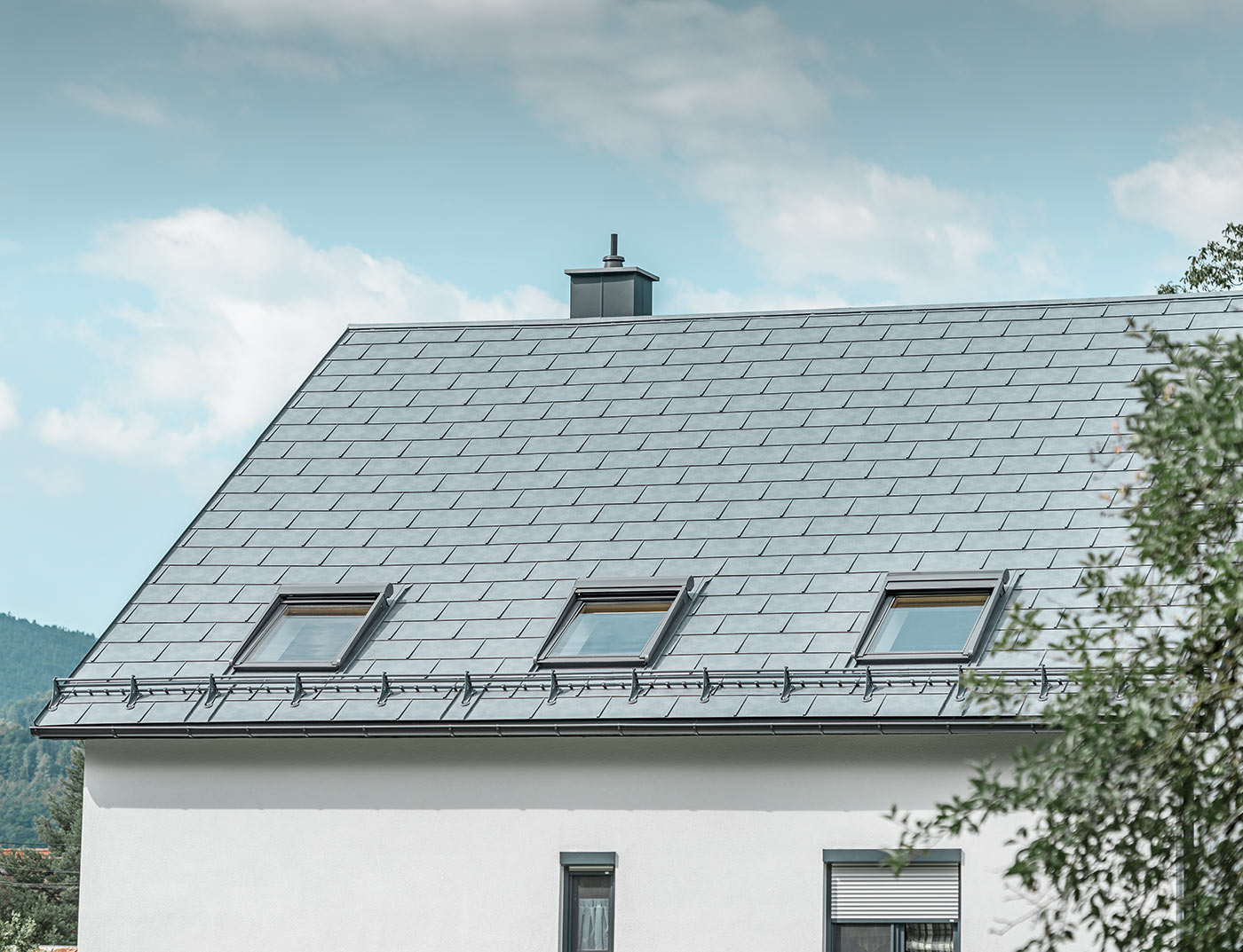 Klassisches Einfamilienhaus mit Satteldach und drei Dachfenstern, eingedeckt mit der Dachplatte R.16 in Steingrau und einer weißen Putzfassade